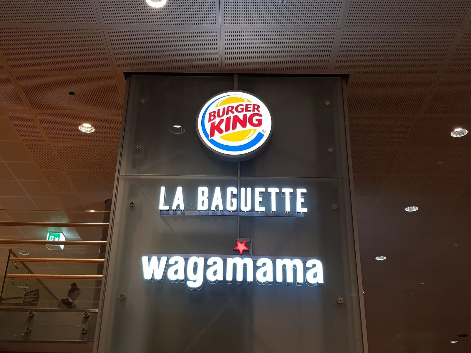 Innendørs skiltsøyle med tre opplyste skilt: Burger King, La Baguette og wagamama